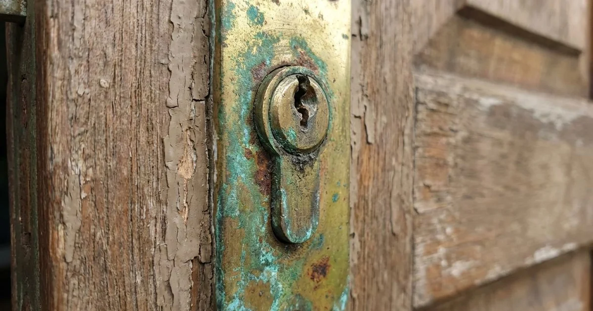 Close-up of a worn and corroded lock cylinder on a residential door showing visible signs of deterioration